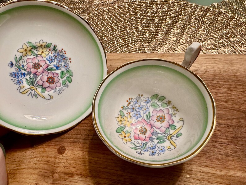 May include: A vintage teacup and saucer set with a green and white floral design. The floral pattern features pink, yellow, and blue flowers.