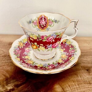 May include: A vintage teacup and saucer set. The teacup and saucer feature a burgundy background with a floral pattern in pink, yellow, and blue. The cup has a gold handle and trim.