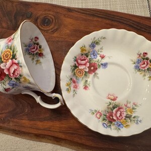 May include: A white teacup and saucer with a floral pattern. The pattern features pink, red, yellow, and blue flowers on a white background.