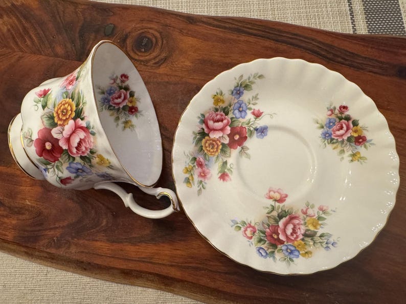 May include: A white teacup and saucer with a floral pattern. The pattern features pink, red, yellow, and blue flowers on a white background.