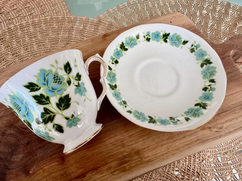 May include: A white teacup and saucer with a floral pattern in shades of blue and green. The floral design features stylised leaves and flowers.