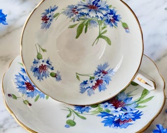 May include: A vintage teacup and saucer set with a delicate floral pattern. The set features a white background with blue and red flowers, accented with gold trim.