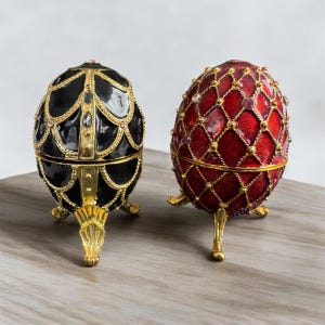 May include: Two decorative egg-shaped boxes with intricate designs. One box is black with gold accents and the other is red with gold accents. Both boxes have three gold legs.