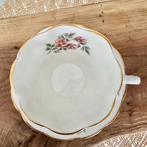May include: A white teacup and saucer with a gold rim and a floral design featuring pink flowers and green leaves.