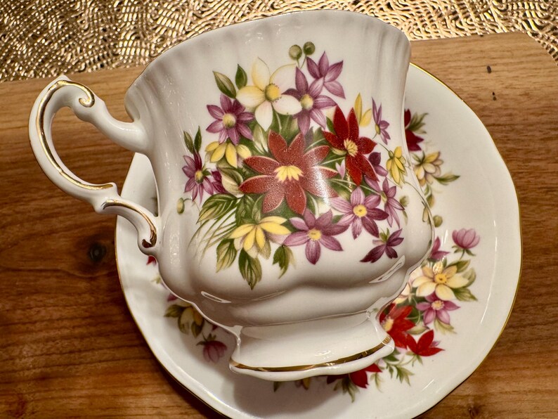 May include: A white teacup and saucer set with a floral design. The cup and saucer feature a delicate floral pattern with red, pink, yellow, and green flowers.