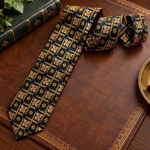 May include: A necktie featuring a dark green background with a repeating geometric pattern of gold floral motifs and small blue diamond shapes. The tie is constructed with a pointed end and a folded upper section, displaying a consistent woven texture.