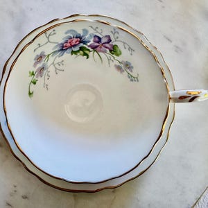 Pu&ograve; includere: Tazza da t&egrave; bianca con bordo smerlato e finiture dorate. Presenta un motivo floreale con fiori blu, viola e rosa. Il manico &egrave; bianco con dettagli dorati. Un classico per t&egrave; o caff&egrave;.