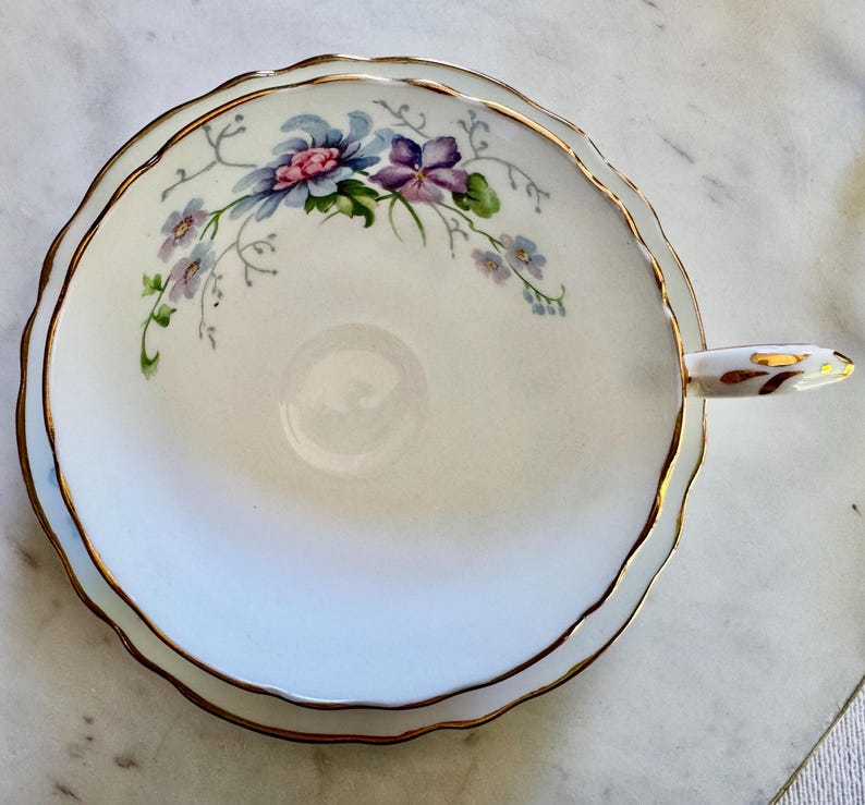 Pu&ograve; includere: Tazza da t&egrave; bianca con bordo smerlato e finiture dorate. Presenta un motivo floreale con fiori blu, viola e rosa. Il manico &egrave; bianco con dettagli dorati. Un classico per t&egrave; o caff&egrave;.