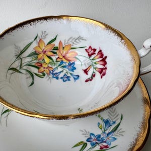 May include: A white teacup and saucer with a gold rim and floral pattern. The flowers are pink, yellow, and blue.