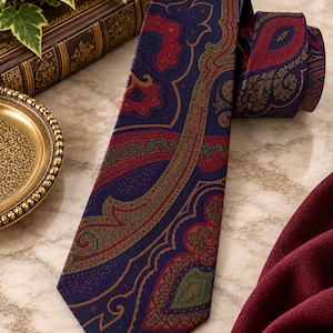 Pode incluir: Uma gravata com base azul-escura e um intrincado padr&atilde;o paisley em tons de vermelho profundo, verde-oliva e dourado. O tecido apresenta uma textura lisa com um design ornamental repetitivo que cobre todo o comprimento da gravata.