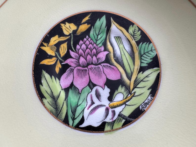 May include: A black and white floral design with pink, yellow, and green accents. The design is surrounded by a gold border and the signature "A.Bentille" is visible in the lower right corner.