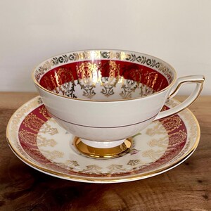 Pode incluir: Conjunto de ch&aacute; vintage branco com design vermelho e dourado. A ch&aacute;vena tem uma pega dourada e assenta num pires a condizer. O conjunto apresenta um design ornamental, ideal para a hora do ch&aacute;.