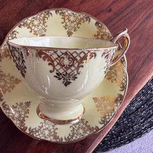 May include: A vintage teacup and saucer set with a pale yellow background and gold filigree design.