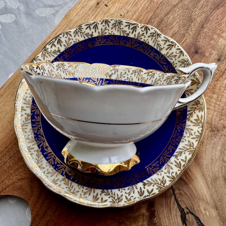 May include: A white teacup and saucer with a blue and gold floral pattern. The saucer has a scalloped edge.
