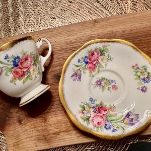 May include: A white teacup and saucer with a gold rim and floral pattern. The flowers are pink, purple, and yellow.