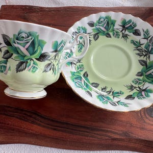 May include: A green and white teacup and saucer set with a floral pattern. The cup and saucer feature a delicate green and white floral design with a gold trim.