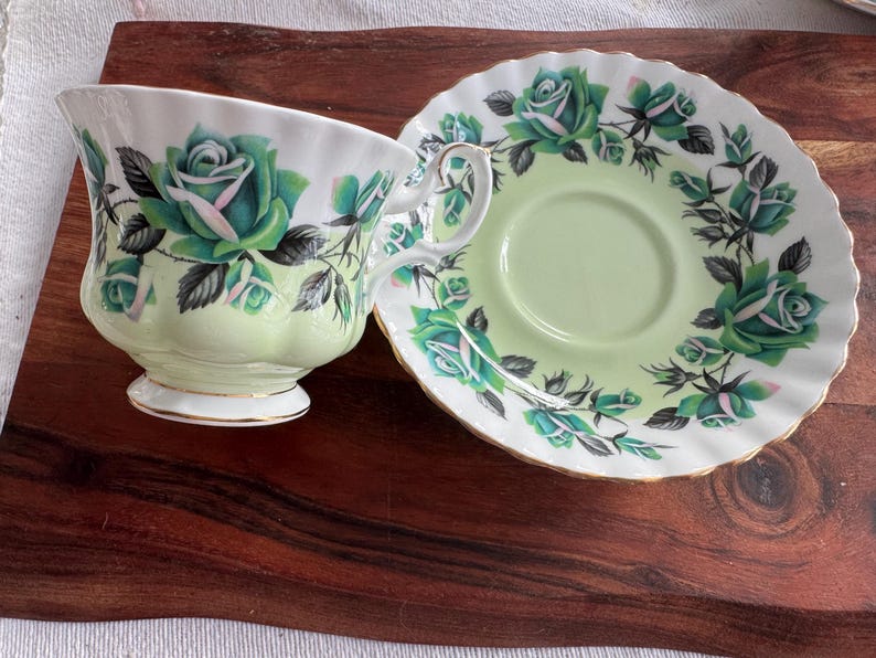 May include: A green and white teacup and saucer set with a floral pattern. The cup and saucer feature a delicate green and white floral design with a gold trim.