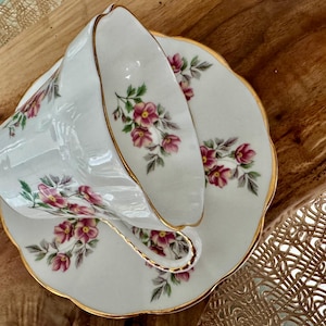 May include: A white teacup and saucer set with a floral pattern of pink and green flowers. The set has a gold trim around the edges.