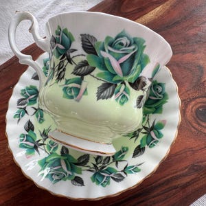 May include: A green and white teacup and saucer set with a floral pattern. The cup and saucer are decorated with green roses and leaves.