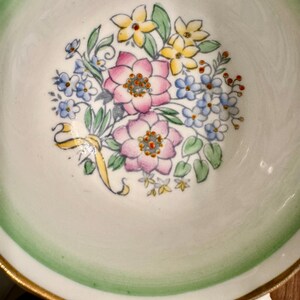 May include: A vintage teacup with a green rim and gold trim. The inside of the cup features a floral design with pink, yellow, and blue flowers.
