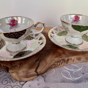 Puede incluir: Dos tazas de t&eacute; y platillos blancos con ribetes dorados y un dise&ntilde;o de rosas. Las tazas tienen un acabado nacarado y se asientan sobre platillos a juego con un dise&ntilde;o calado decorativo. El juego est&aacute; sobre una superficie de madera.