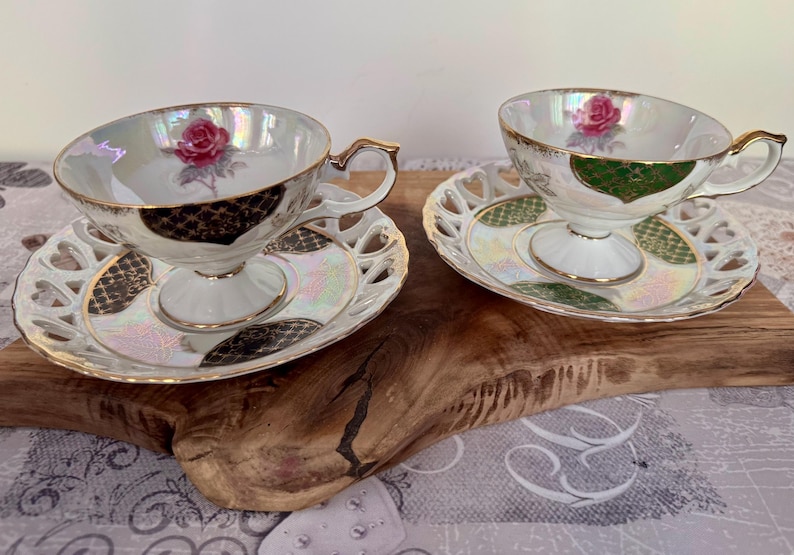 Puede incluir: Dos tazas de t&eacute; y platillos blancos con ribetes dorados y un dise&ntilde;o de rosas. Las tazas tienen un acabado nacarado y se asientan sobre platillos a juego con un dise&ntilde;o calado decorativo. El juego est&aacute; sobre una superficie de madera.