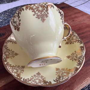 May include: A yellow teacup and saucer with a gold floral pattern. The cup has a gold rim and the saucer has a scalloped edge.