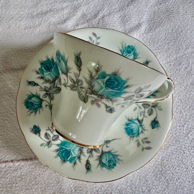 Peut inclure: Service &agrave; th&eacute; blanc avec une tasse et une soucoupe orn&eacute;es de roses turquoise et de bordures dor&eacute;es. L'ensemble pr&eacute;sente un motif floral. Il s'agit probablement d'un service ancien.