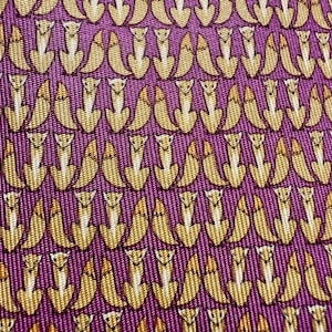 Puede incluir: Una tela de color p&uacute;rpura con un patr&oacute;n repetitivo de peque&ntilde;os zorros estilizados de color marr&oacute;n dorado. Los zorros est&aacute;n representados en posici&oacute;n sentada, dispuestos en filas uniformes sobre el material texturizado.