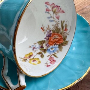 May include: A turquoise teacup and saucer set with a floral design. The cup has a gold rim and the saucer has a scalloped edge.