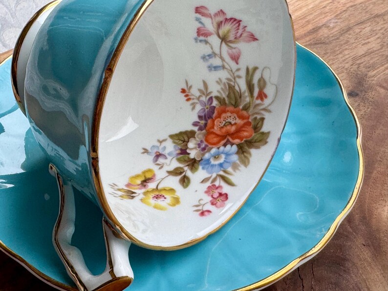 May include: A turquoise teacup and saucer set with a floral design. The cup has a gold rim and the saucer has a scalloped edge.