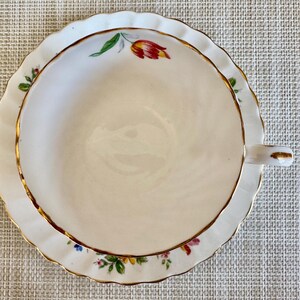 Puede incluir: Una taza de t&eacute; y un platillo blancos con un borde dorado y un patr&oacute;n floral. El platillo tiene un borde festoneado.