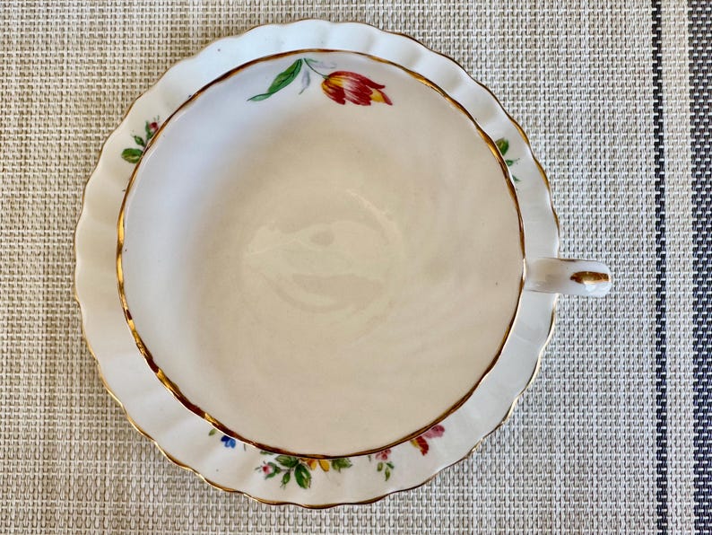 Puede incluir: Una taza de t&eacute; y un platillo blancos con un borde dorado y un patr&oacute;n floral. El platillo tiene un borde festoneado.