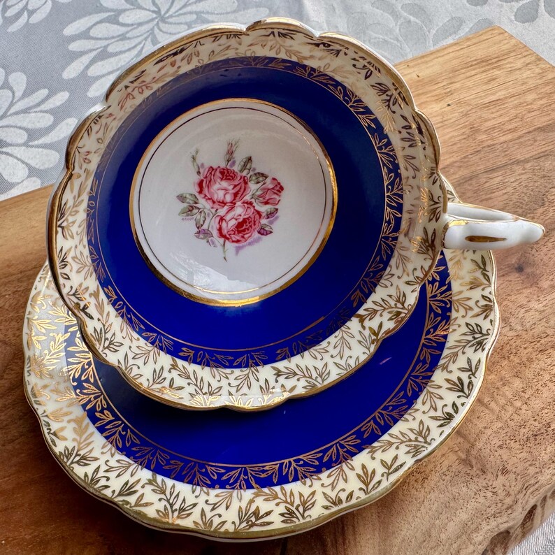 May include: A vintage teacup and saucer set with a cobalt blue base and gold trim. The cup features a delicate floral design with pink roses.