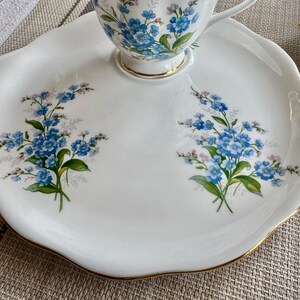 May include: A white porcelain teacup and saucer set with a gold rim. The set features a floral design with blue forget-me-not flowers.