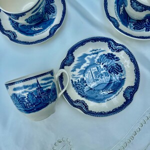 Puede incluir: Un juego de tazas y platillos vintage azules y blancos. Cada pieza presenta una escena de paisaje detallada con una iglesia y &aacute;rboles. Los bordes tienen un borde decorativo. El juego est&aacute; dispuesto sobre una superficie blanca.