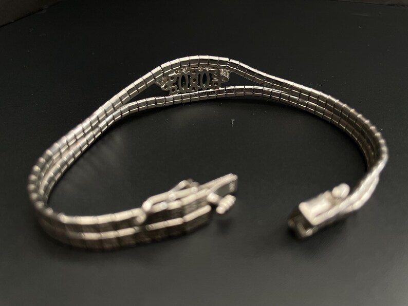 May include: A silver bracelet with a triple row chain design. The bracelet has a clasp closure and features the word "XOXO" in the centre.
