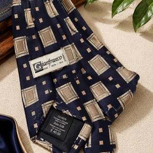 May include: A navy blue silk tie with a repeating pattern of tan squares and smaller tan squares. The tie has a label that reads "Gianfranco" and "Soie Seta Silk". The tag also indicates the tie is made in Canada and is silk.