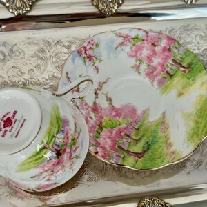 May include: A vintage teacup and saucer set with a floral design. The white porcelain cup and saucer feature pink blossoms, green foliage, and a gold trim. The teacup is marked "Royal Albert Bone China, England."