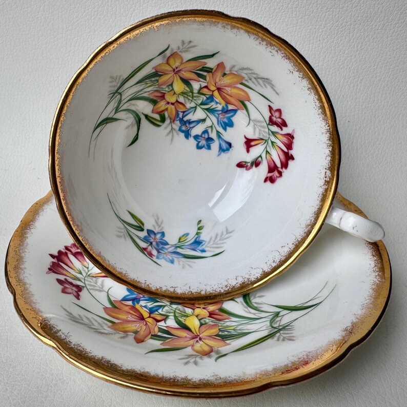 May include: A vintage teacup and saucer set with a floral design. The cup and saucer are white with a gold rim and feature a delicate floral pattern in shades of pink, yellow, and blue.