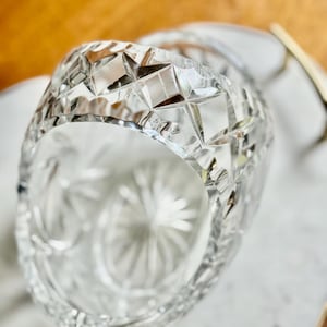 May include: A clear, cut-glass bowl with a geometric pattern. The bowl's rim features a series of diamond shapes, and the interior has a starburst design. The bowl is likely used for serving or display.