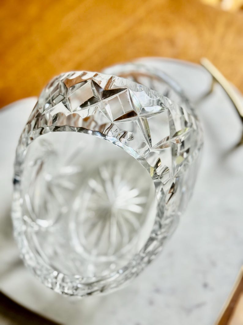 May include: A clear, cut-glass bowl with a geometric pattern. The bowl's rim features a series of diamond shapes, and the interior has a starburst design. The bowl is likely used for serving or display.