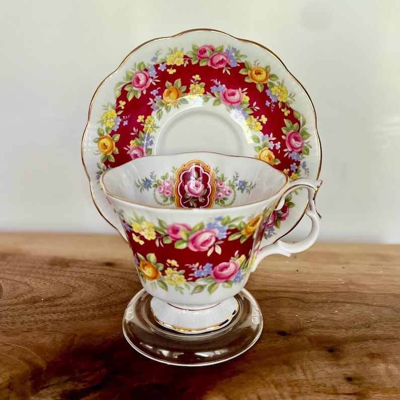 May include: A vintage teacup and saucer set. The teacup and saucer feature a red background with a floral pattern in pink, yellow, and blue. The teacup has a clear glass base and a gold trim.