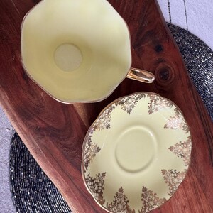 May include: A yellow teacup and saucer set with gold trim and a delicate floral pattern. The cup and saucer are both made of fine china.