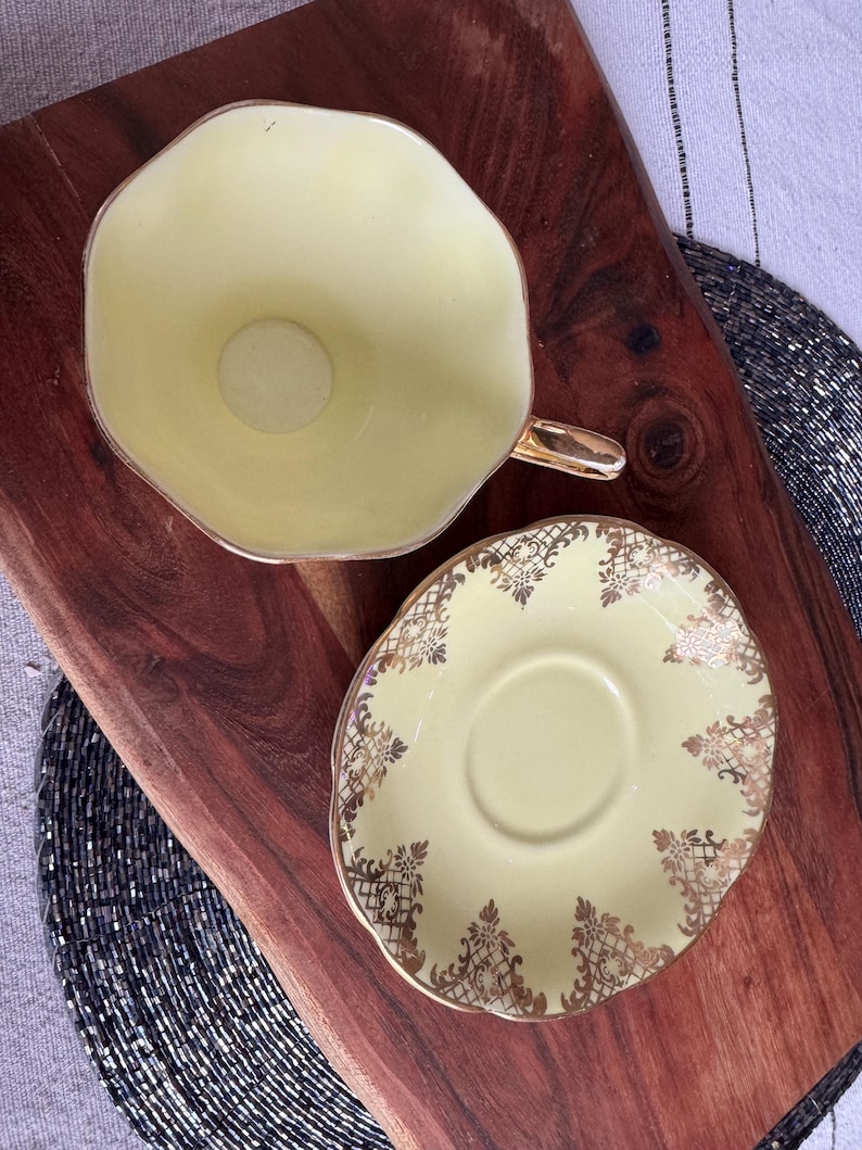 May include: A yellow teacup and saucer set with gold trim and a delicate floral pattern. The cup and saucer are both made of fine china.
