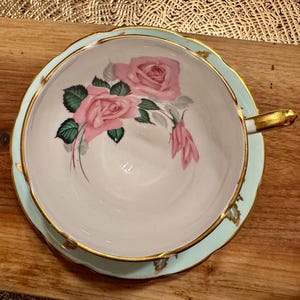 May include: A light blue teacup and saucer with a gold rim. The teacup features a floral design with pink roses and green leaves.