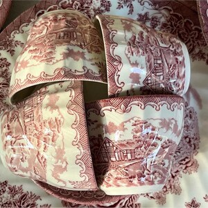 Pu&ograve; includere: Un set di tazze e piattini antichi color crema con un motivo toile rosso. Le tazze e i piattini sono disposti su un vassoio pi&ugrave; grande, anch'esso con lo stesso disegno. Il motivo raffigura un paesaggio rurale.