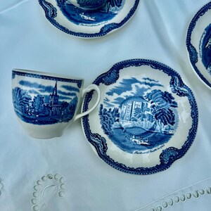 Puede incluir: Un juego de tazas y platillos de cer&aacute;mica azul y blanca con un dise&ntilde;o detallado de paisaje. Las tazas tienen asas y los platillos tienen un borde festoneado. El juego est&aacute; colocado sobre un mantel blanco.