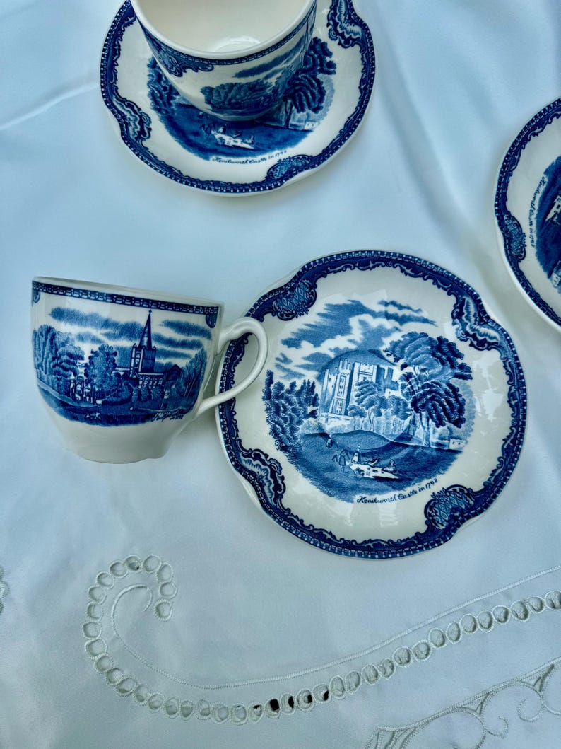 Puede incluir: Un juego de tazas y platillos de cer&aacute;mica azul y blanca con un dise&ntilde;o detallado de paisaje. Las tazas tienen asas y los platillos tienen un borde festoneado. El juego est&aacute; colocado sobre un mantel blanco.