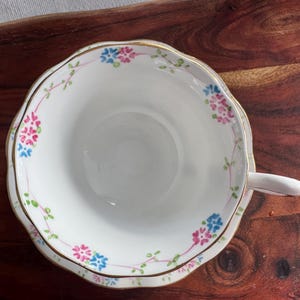 May include: A white teacup and saucer with a gold rim and a floral pattern in pink, blue, and green.